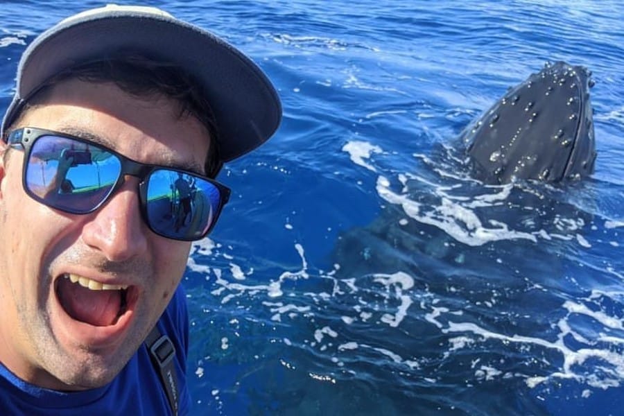 A guest grinning as a humpback whale surfaces right beside the boat off Maui